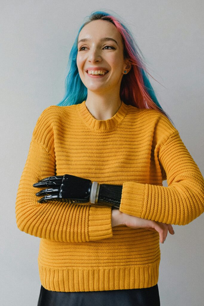 pexels-photo-3732881-3732881 Cheerful woman with pink and blue hair wearing a prosthetic arm and yellow sweater indoors.