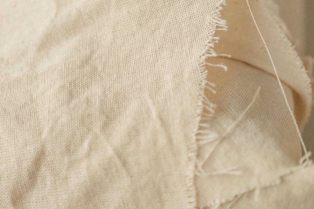 Detailed close-up of beige fabric showcasing frayed edges and texture, ideal for design and textile references.